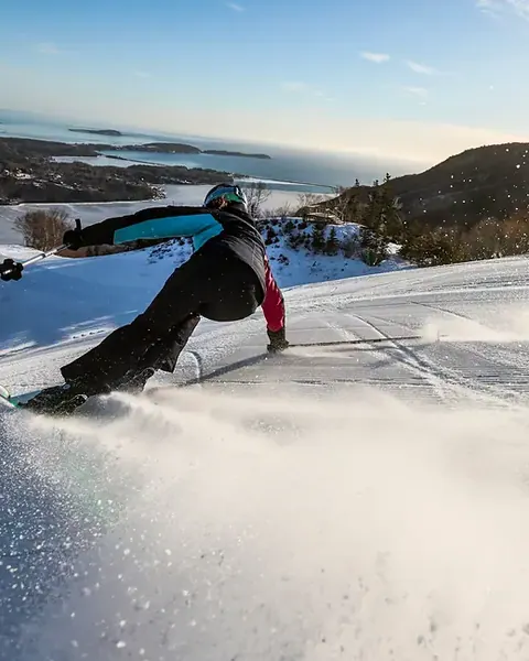 Snowboarder carving a groomed run above the ocean