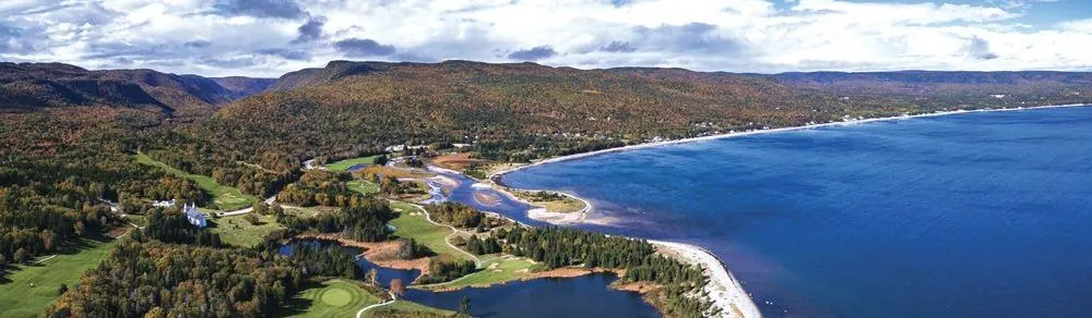 Aerial view of Ingonish: the green peninsula, golf course and long beach between two blue bays