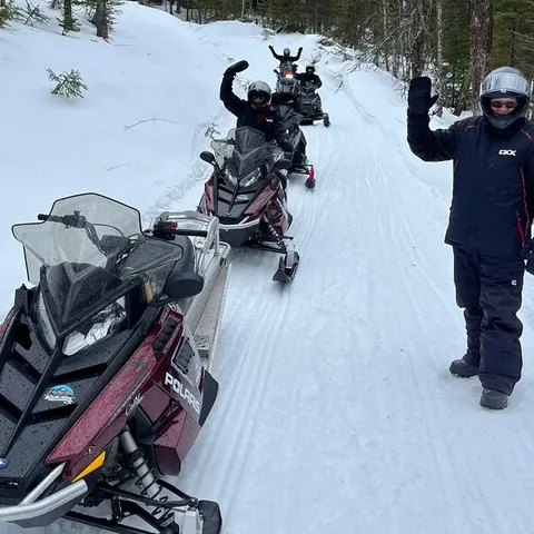 Snowmobiler waving beside parked sleds on a snowy trail