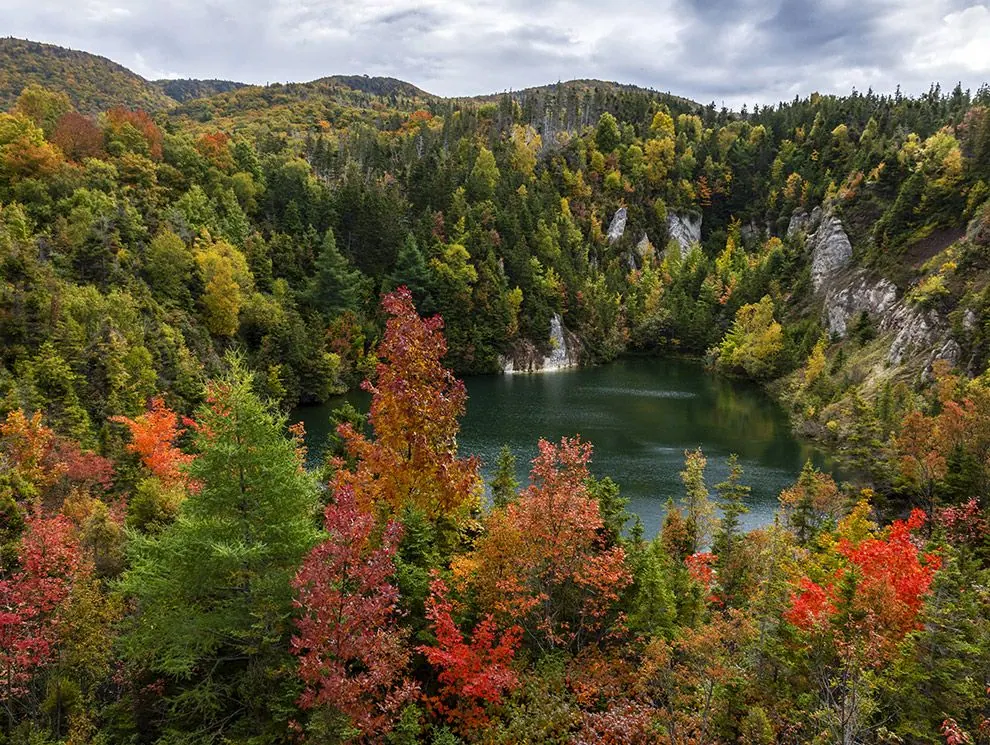 Autumn forest in red, orange and green around a deep green lake in Cape Breton Highlands National Park