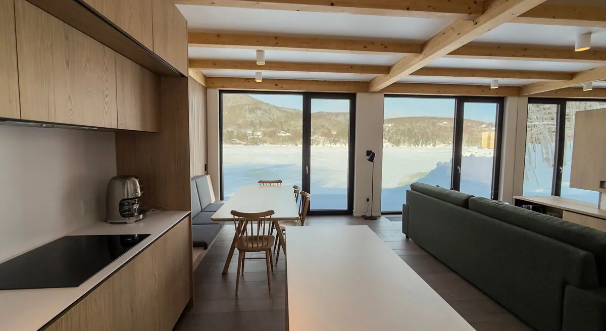 Open-plan living room with sofa, dining table and floor-to-ceiling windows onto the frozen bay
