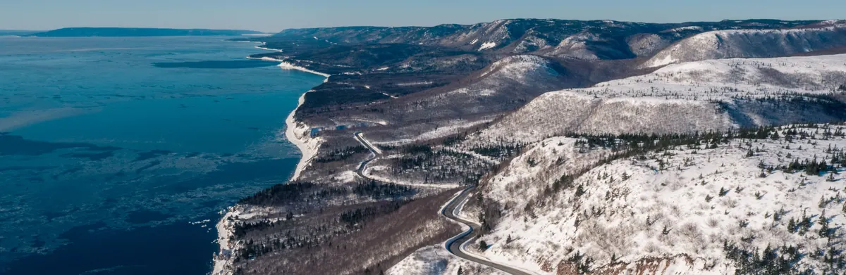 Aerial view of the snowy Cape Breton coast and the winding Cabot Trail above the blue Atlantic