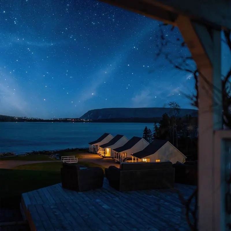 Starry night sky above lit chalets on the shore, seen from a covered porch
