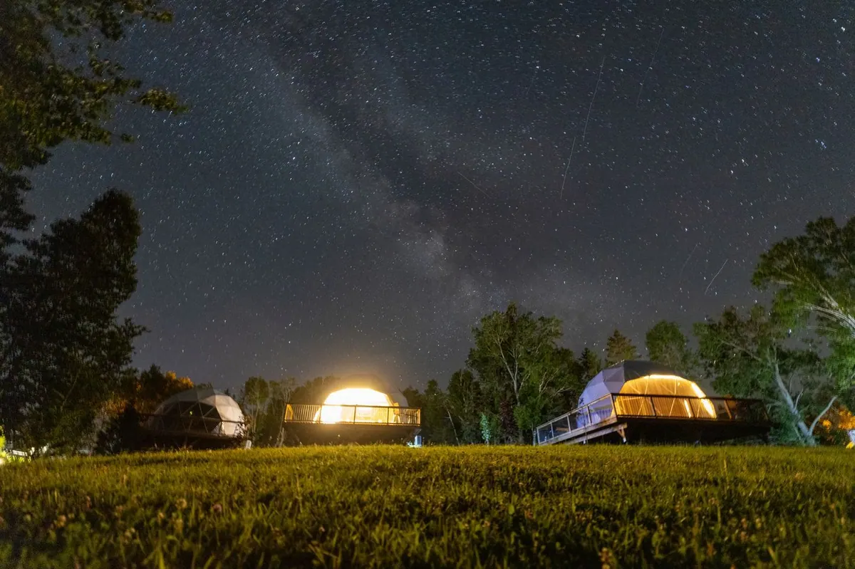 Milky Way above glowing dome tents in a dark meadow