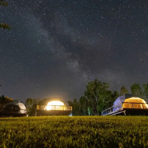 Milky Way above glowing dome tents in a dark meadow