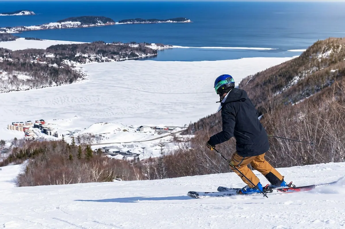 Skier on a groomed run at Cape Smokey with the snowy coastline far below