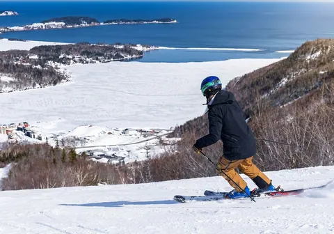 Skier carving down a Cape Smokey run above the frozen bay and Ingonish