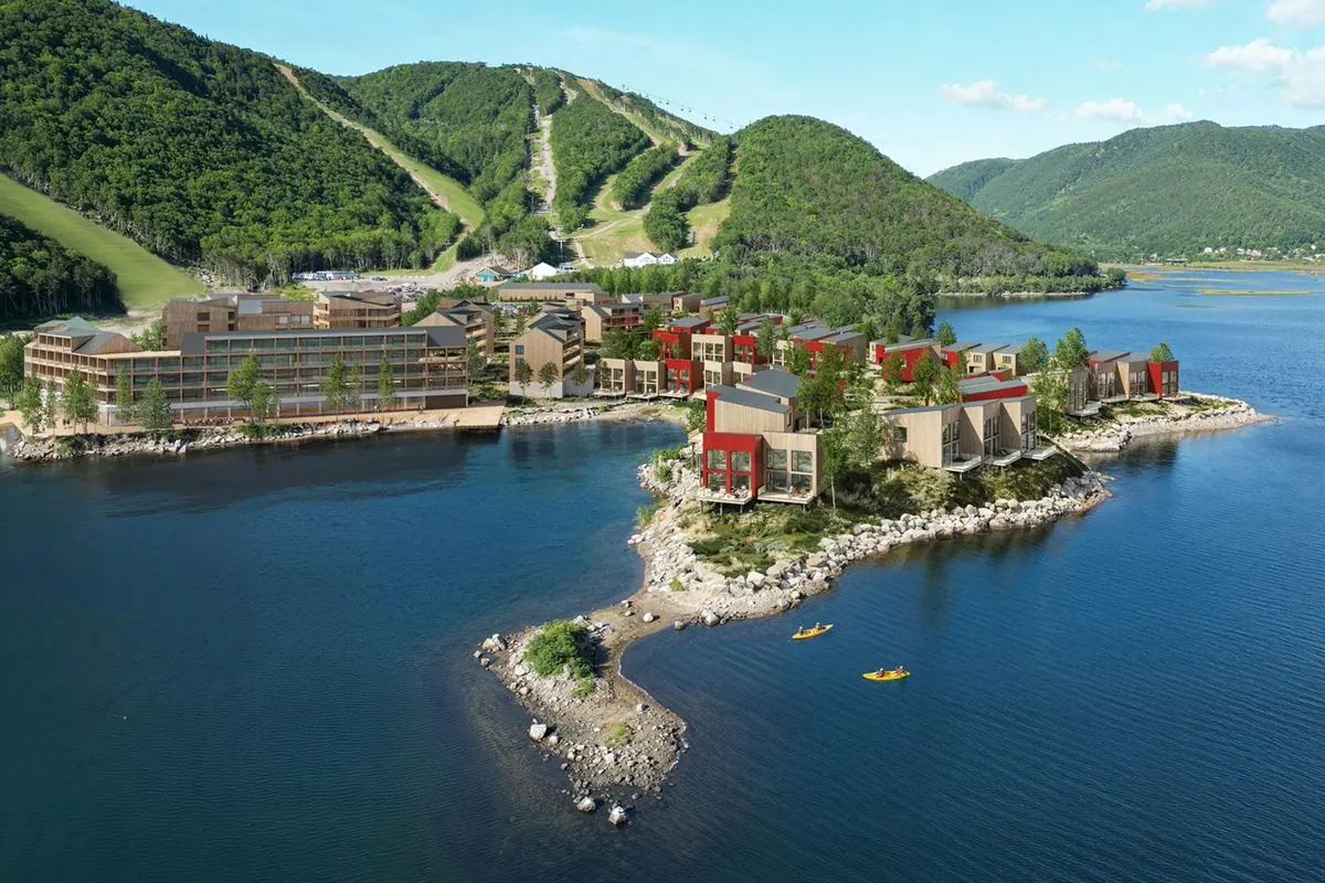 Chalets by the water below green hills in summer