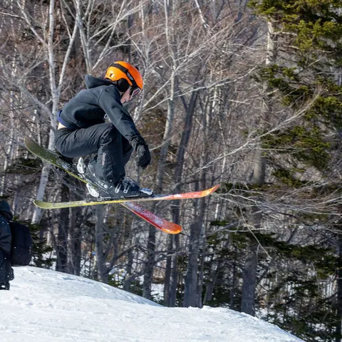 Skier jumping between birch trees while a photographer watches