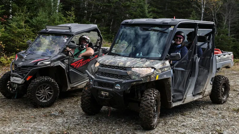 Two side-by-side off-road vehicles with riders in the woods