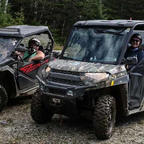 Two side-by-side off-road vehicles with riders in the woods
