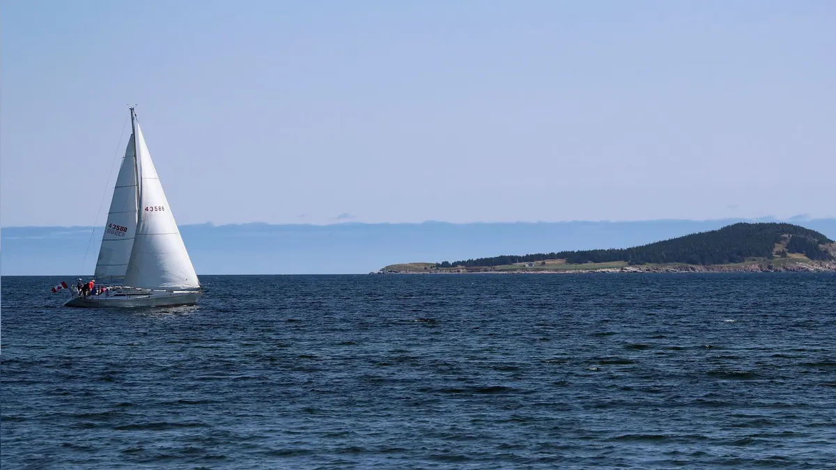 White sailboat on the open Atlantic near a headland